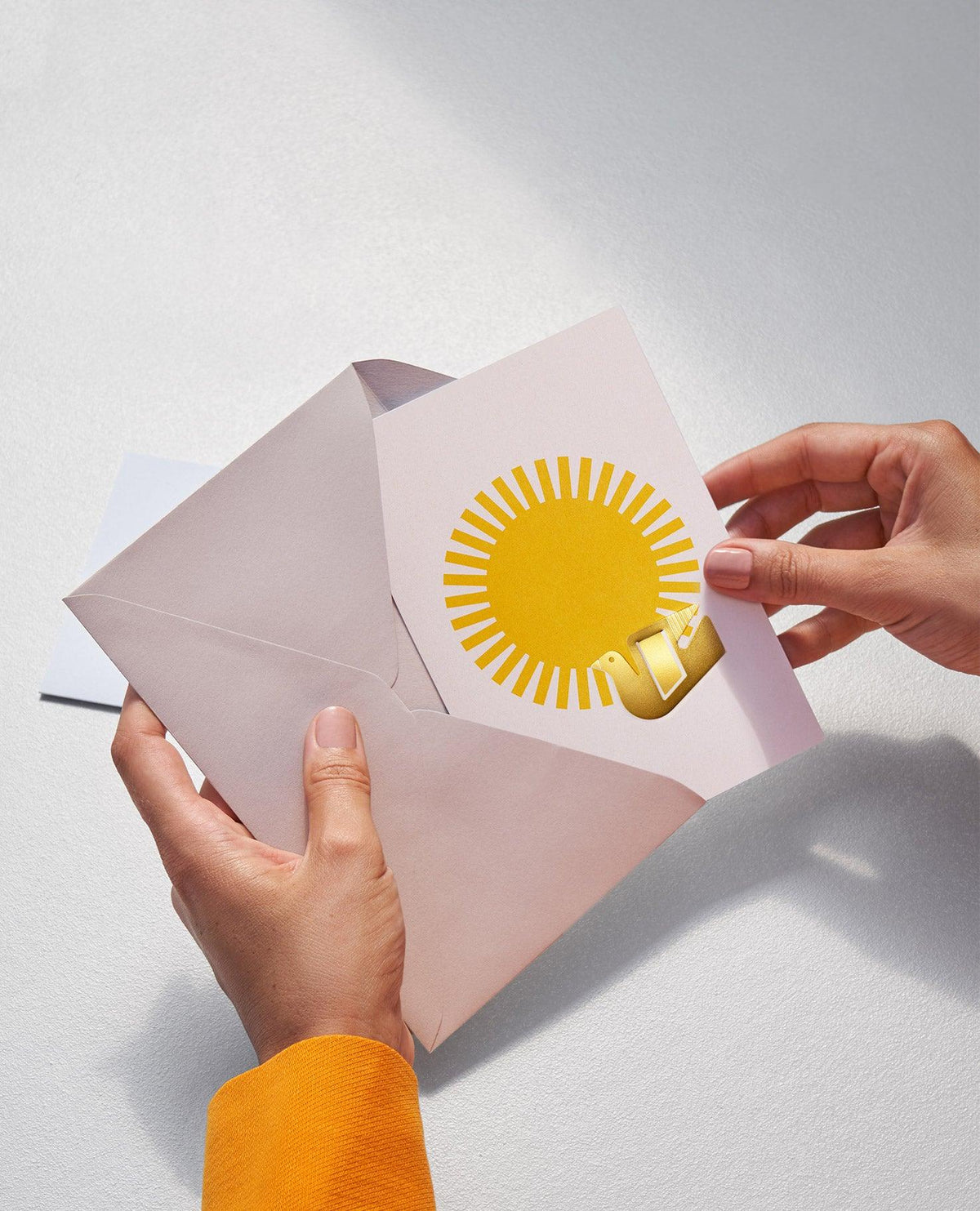 Hands holding an open Dove Greeting Card by OCTAEVO, featuring a yellow sun and a gold bird illustration.