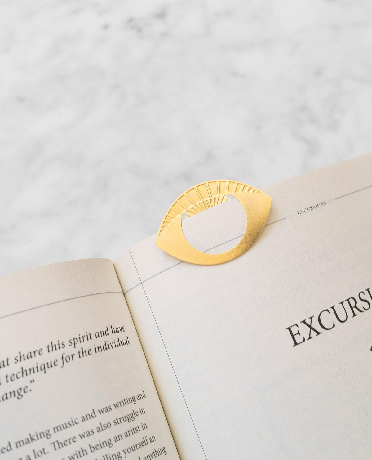 The OCTAEVO Greeting Card, a gold brass eye-shaped clip, rests on an open book over white marble.