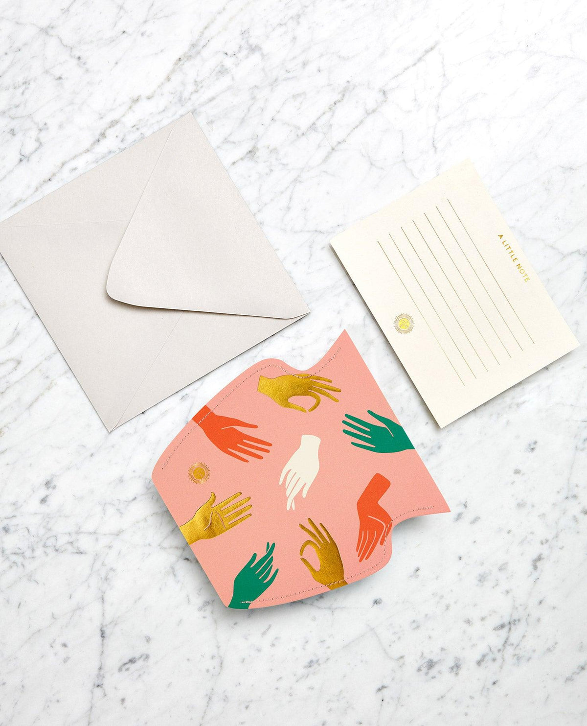 A lined card, gray envelope and pink OCTAEVO Hamsa Mini Paper Vase displayed on a marble surface.