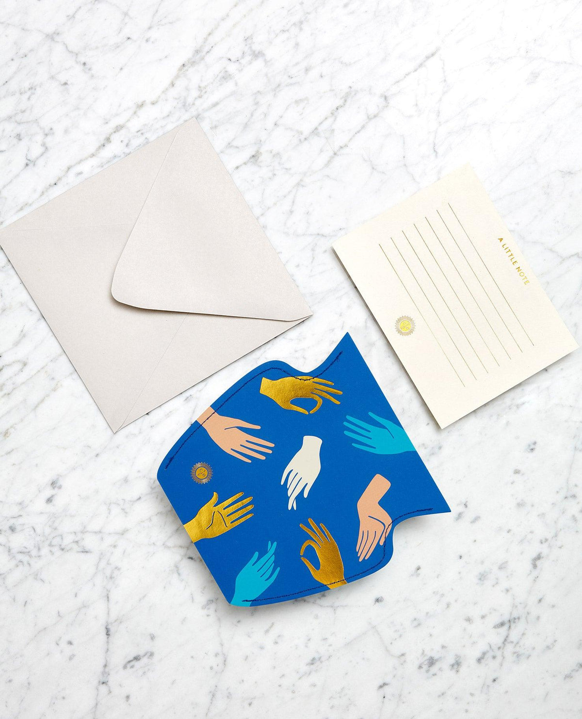 A blue and gold Hamsa Paper Vase by OCTAEVO with greeting card, envelope, and illustrated hands on marble.