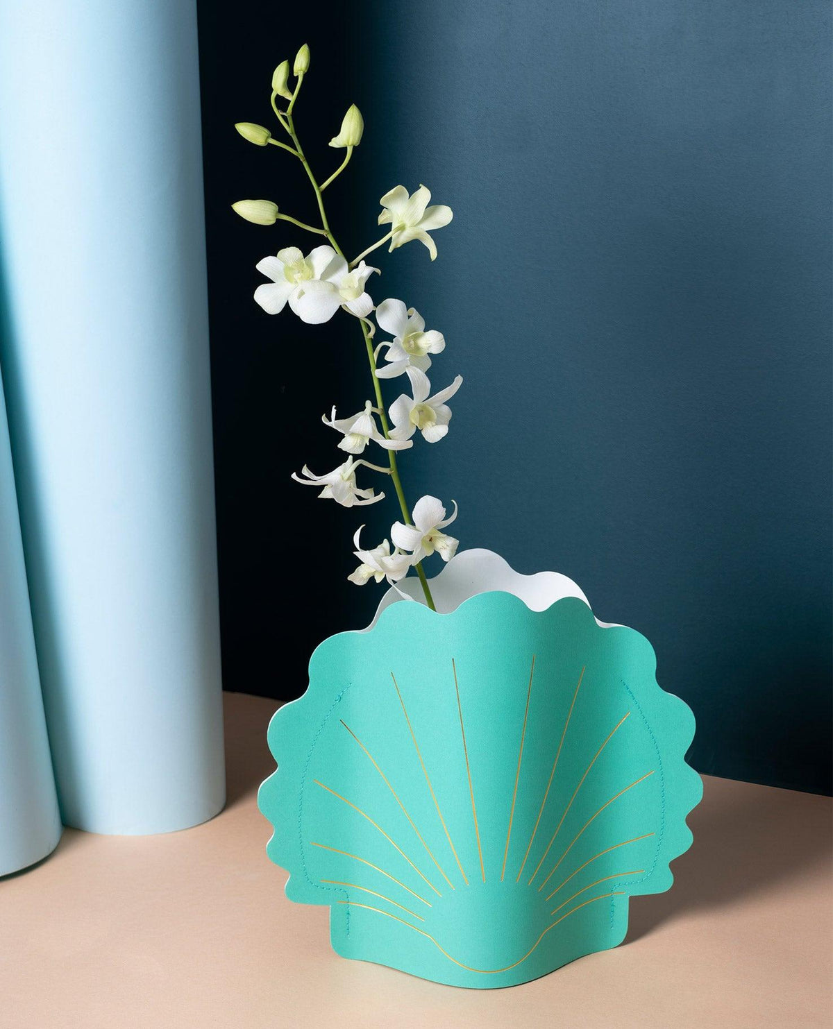 A white orchid in green OCTAEVO’s Hera Paper Vase with gold lines, set against a blue background.