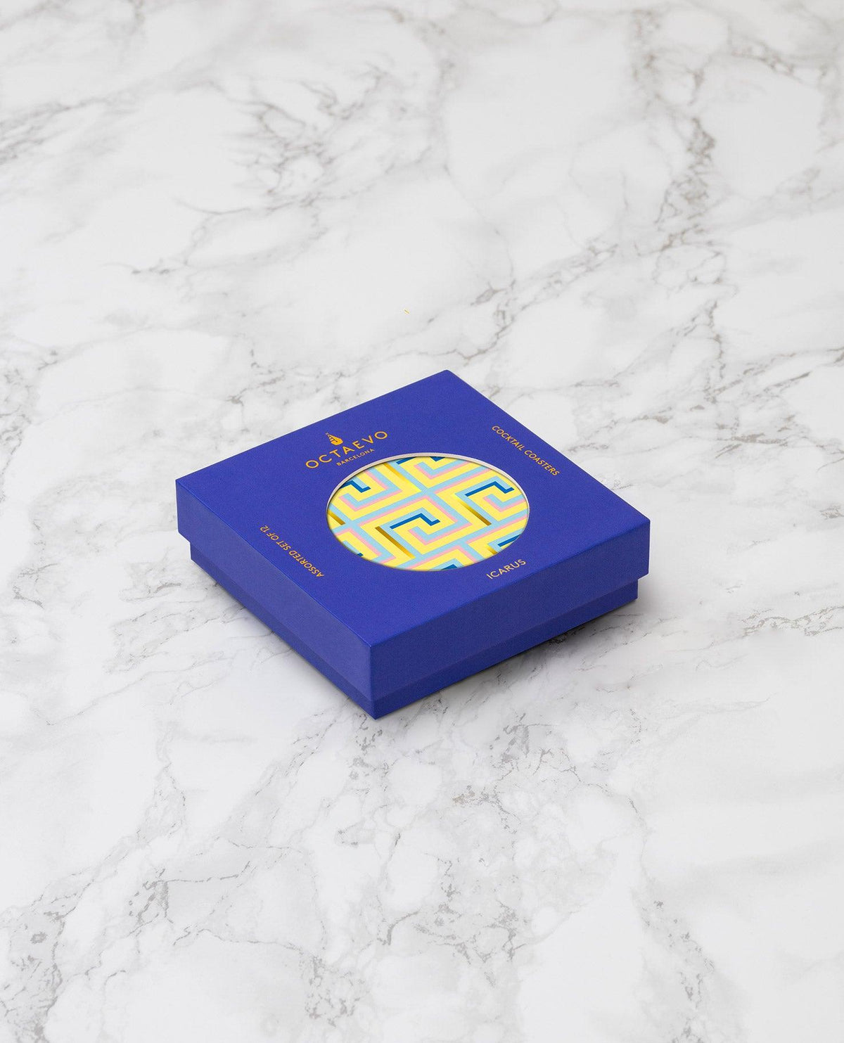 The OCTAEVO Icarus Cocktail Coasters (Set of 12) comes in a blue box with yellow patterns and gold accents.