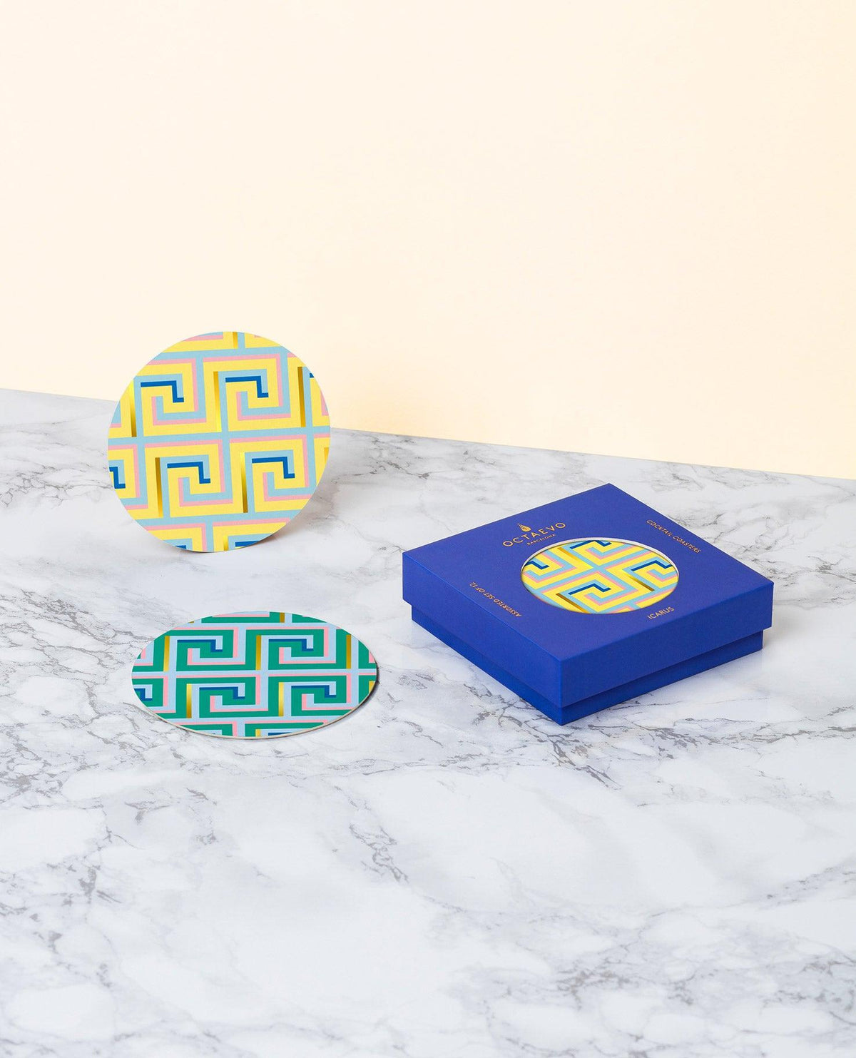 OCTAEVO Icarus Coasters (Set of 12), yellow and green, by a luxe gift box on marble with a beige background.