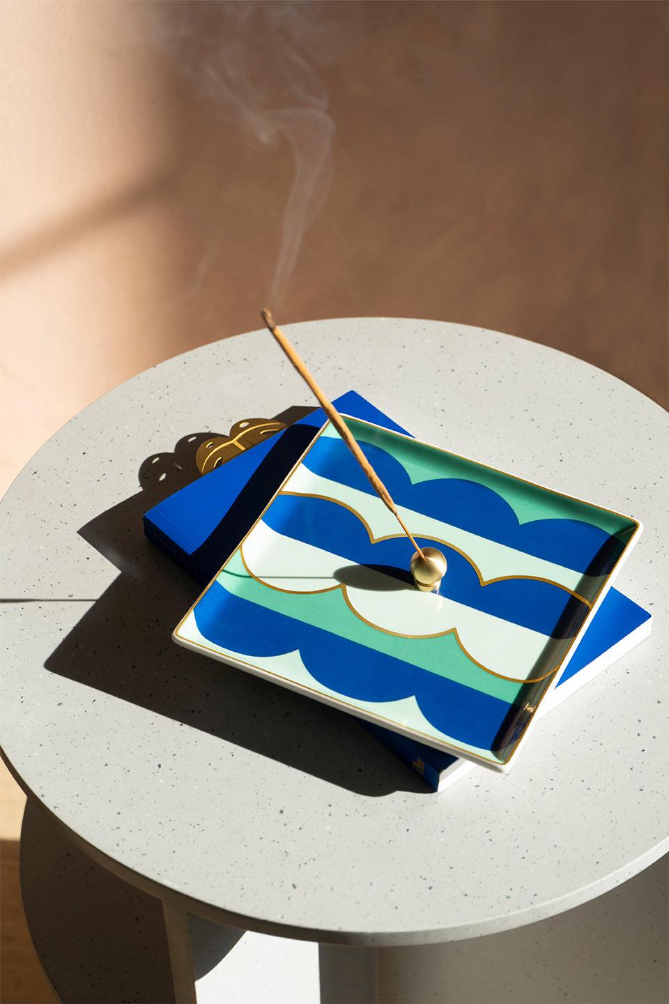 An Octaevo Incense Sticks White Sage burns on a blue-green plate, smoke curling above the white round table.