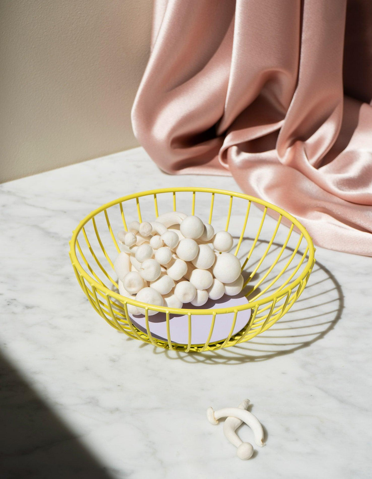 The yellow Iris Wire Basket by OCTAEVO holds mushrooms on marble—a sculptural centerpiece for modern decor.