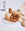 The orange OCTAEVO Iris Wire Basket holds assorted breads and a pretzel, set with milk and beige cloth on white linen.