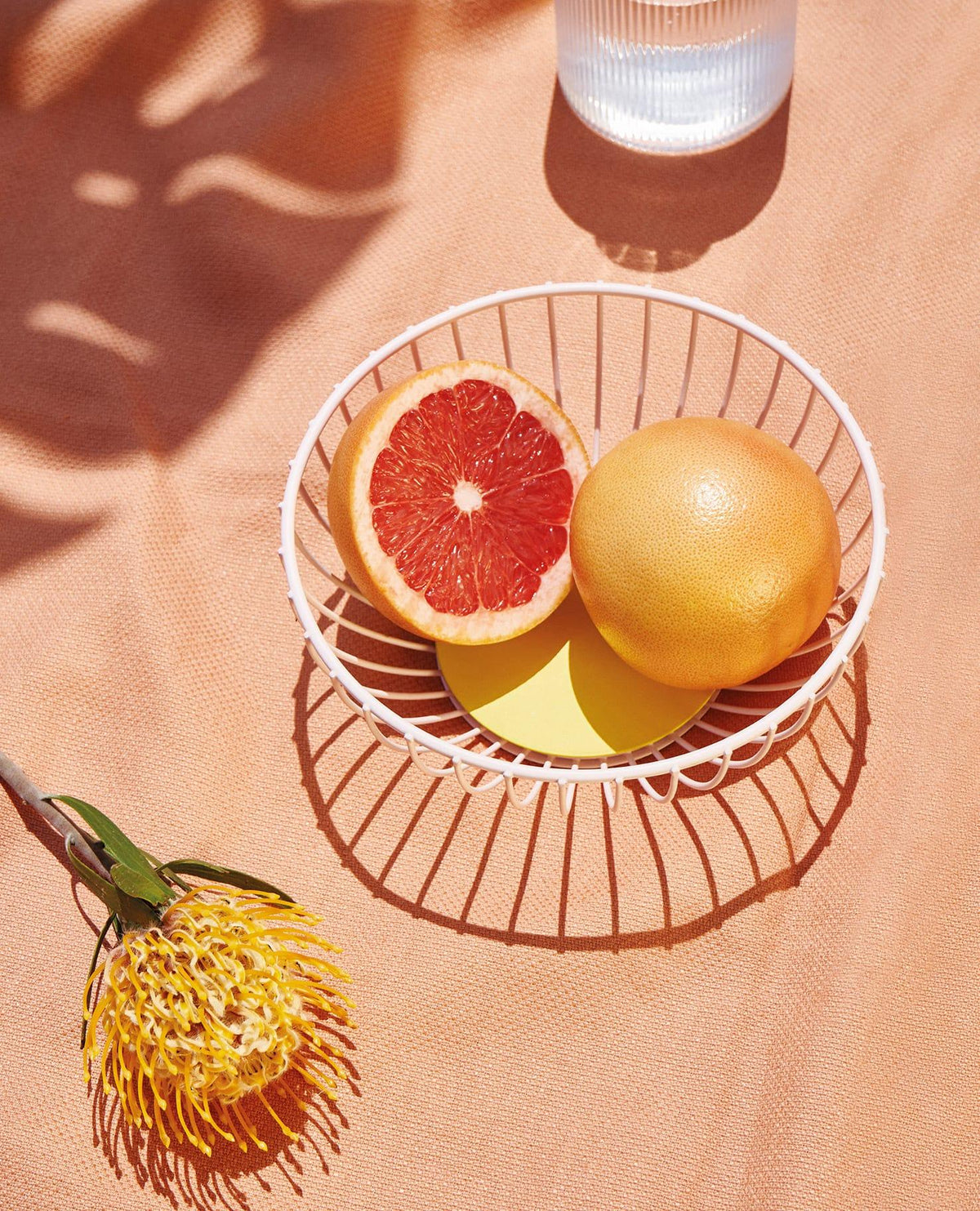 The pink OCTAEVO Iris Wire Basket with grapefruit sits on peach cloth, a centerpiece for modern decor.