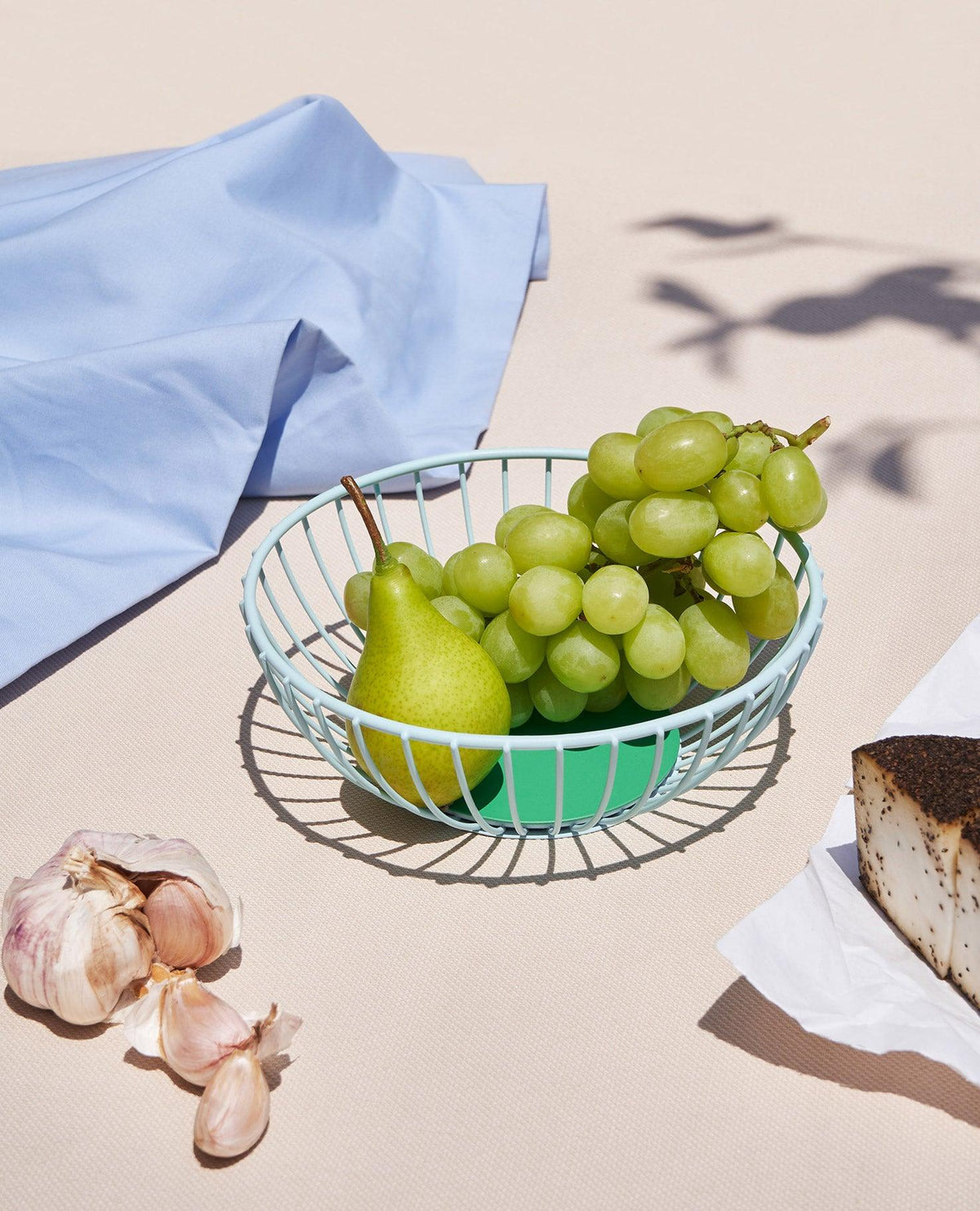 The light blue OCTAEVO Iris Wire Basket with green grapes and a pear make a striking centerpiece. 