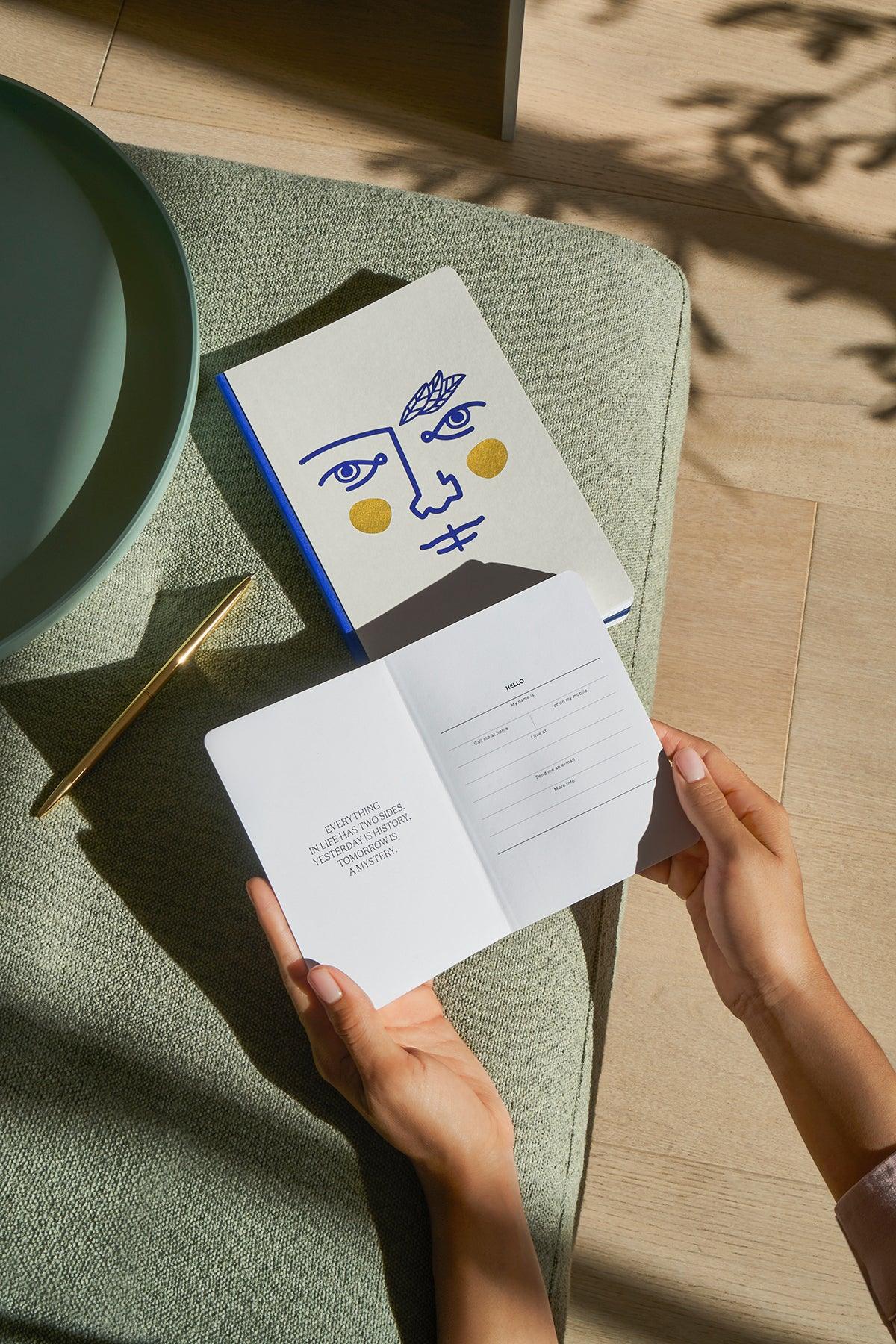Hands holding an open luxury notebook beside a closed Octaevo Janus Notes A6 and pen on a tray.