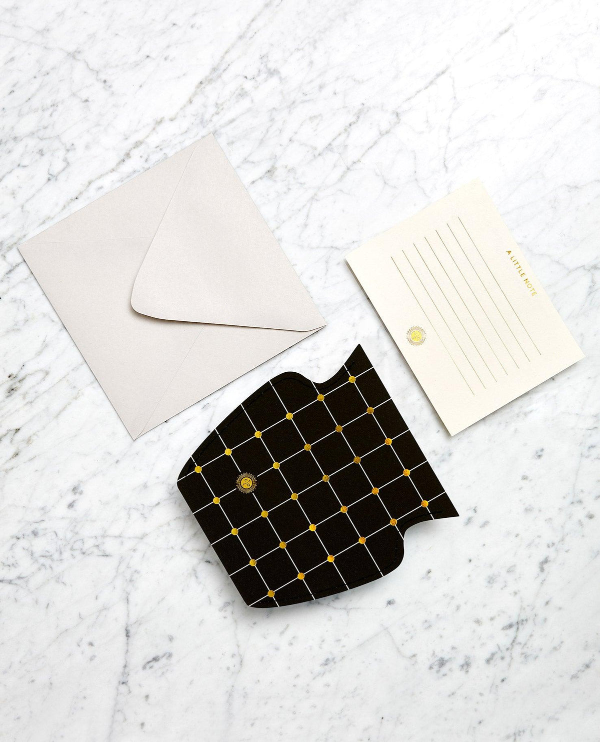 Une enveloppe et une carte sont posées à côté du vase en papier Lido noir et or d'OCTAEVO, sur une surface en marbre.
