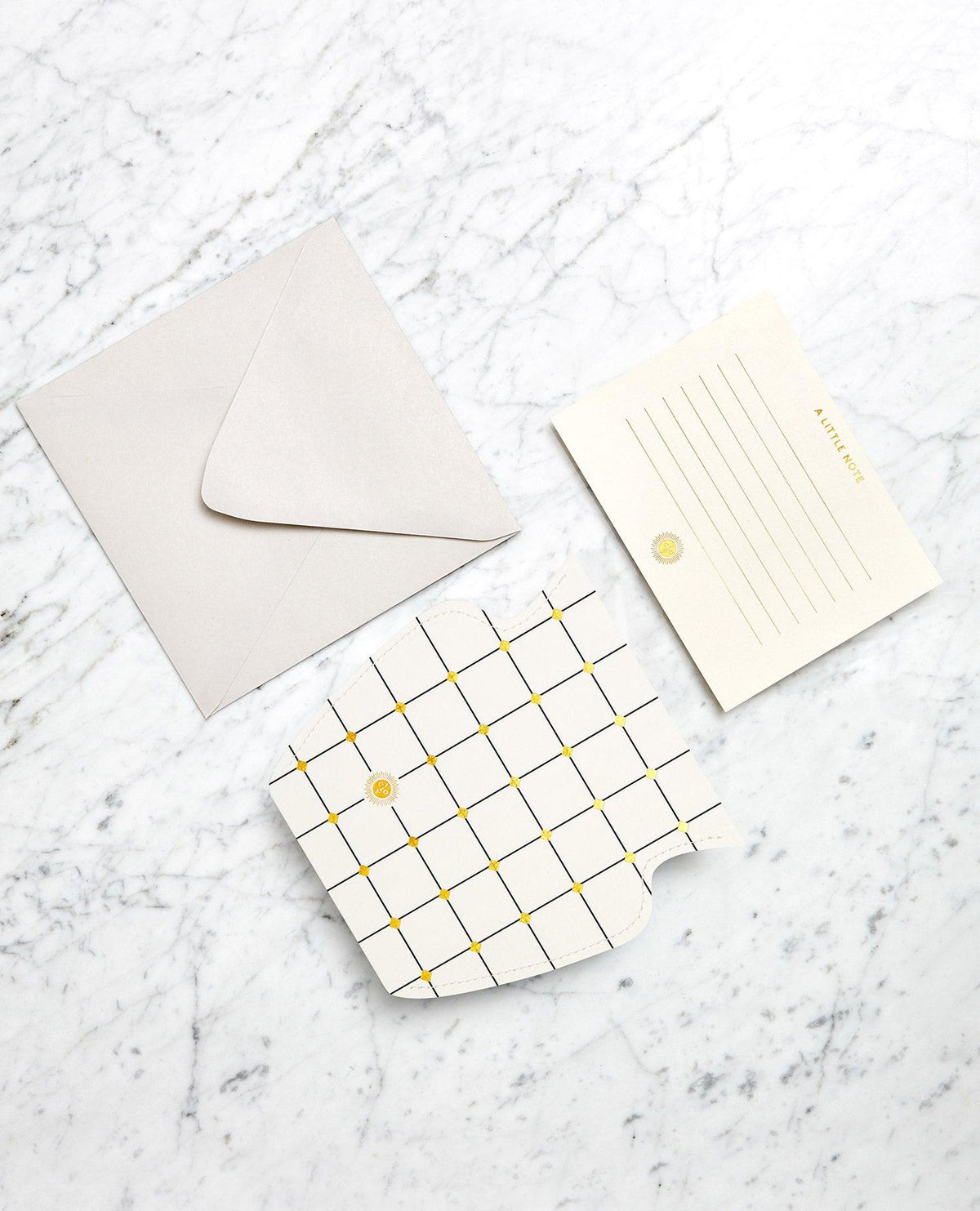 Une carte à liseré doré avec une enveloppe grise est posée à côté du vase en papier Lido OCTAEVO blanc, sur une surface en marbre.