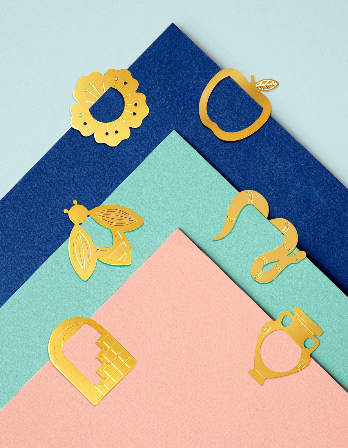 OCTAEVOs Capri Metallclips glänzen vor geschichteten pastellfarbenen und marineblauen Hintergründen, kombiniert mit goldenen Metallic-Lesezeichen.