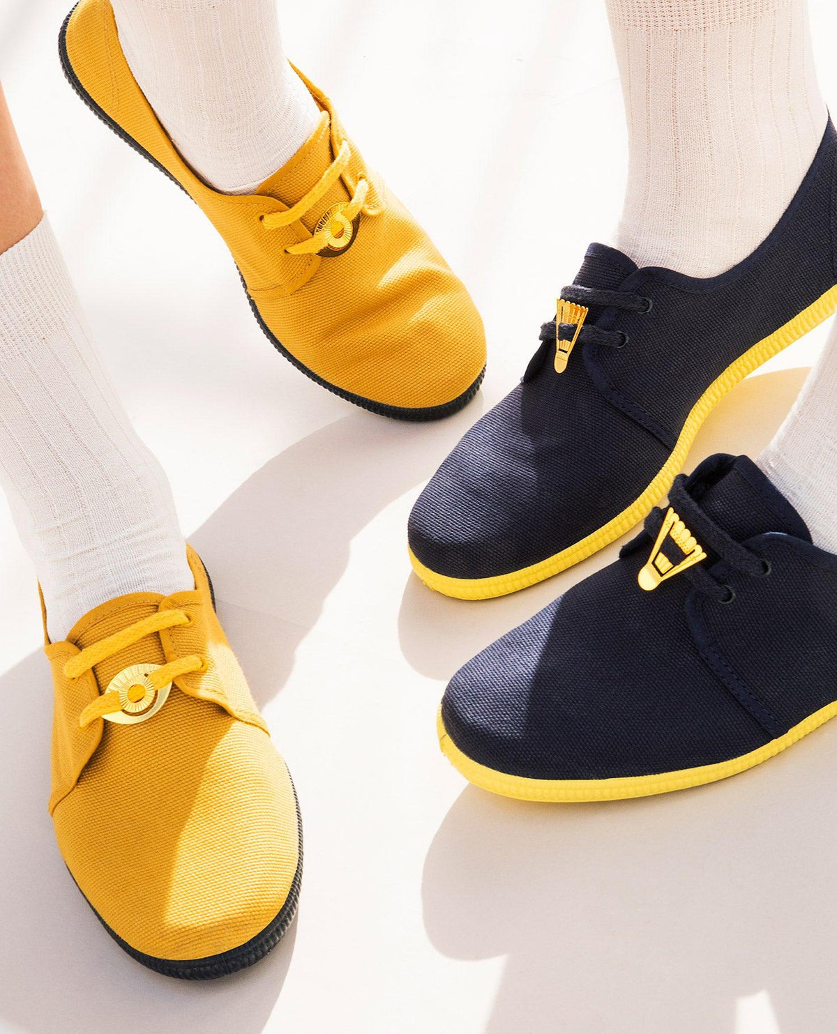 Deux personnes en chaussettes blanches et baskets ornées de clips métalliques Talisman OCTAEVO aux accents jaunes se tiennent sur un sol clair.