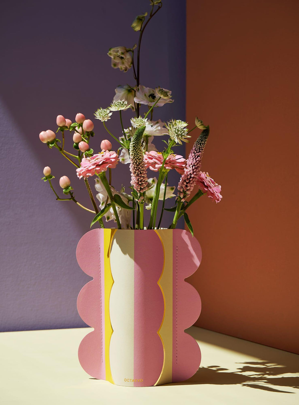 The Mini Paper Vase Riviera Wave by OCTAEVO features scalloped edges in pastel pink and yellow for a bold accent.