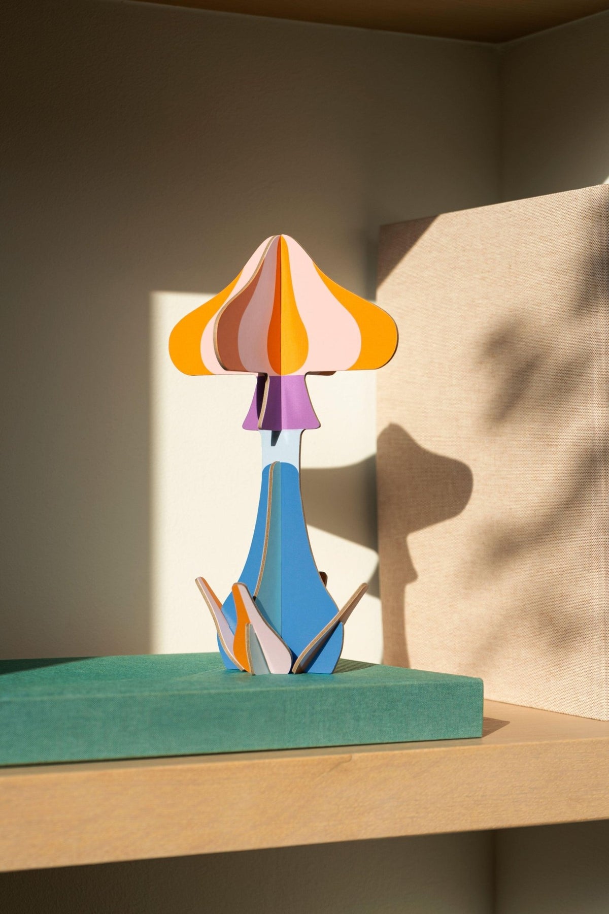 Octaevo Mushroom Paper Sculpture 3 displayed on a shelf with sunlight casting colorful abstract shadows on the wall.