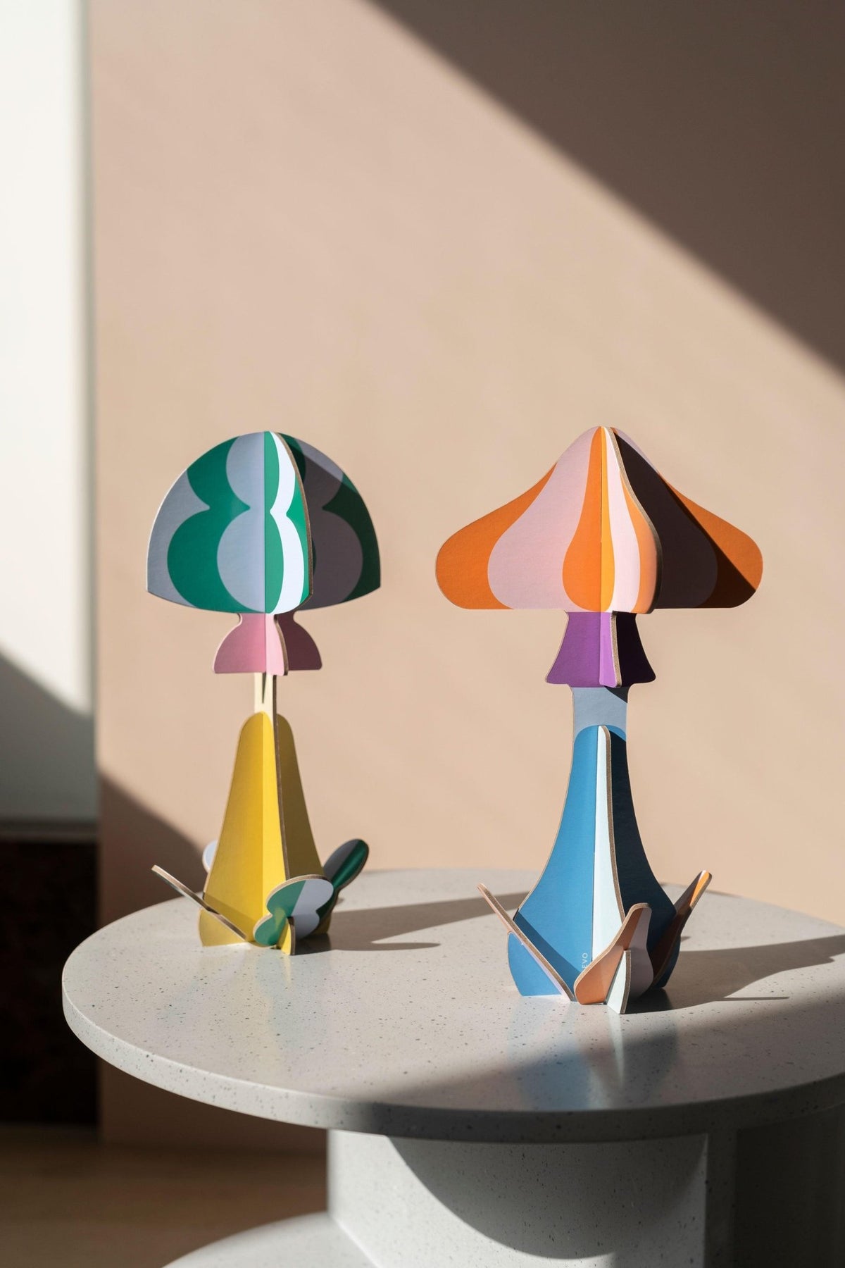 Two Willow Mushroom Paper Sculptures by OCTAEVO sit on a round light gray table in soft sunlight.