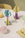 Octaevos Mushroom Paper Sculpture 4, drinks, and fruit sit on a beige dining table with a yellow chair in the background.