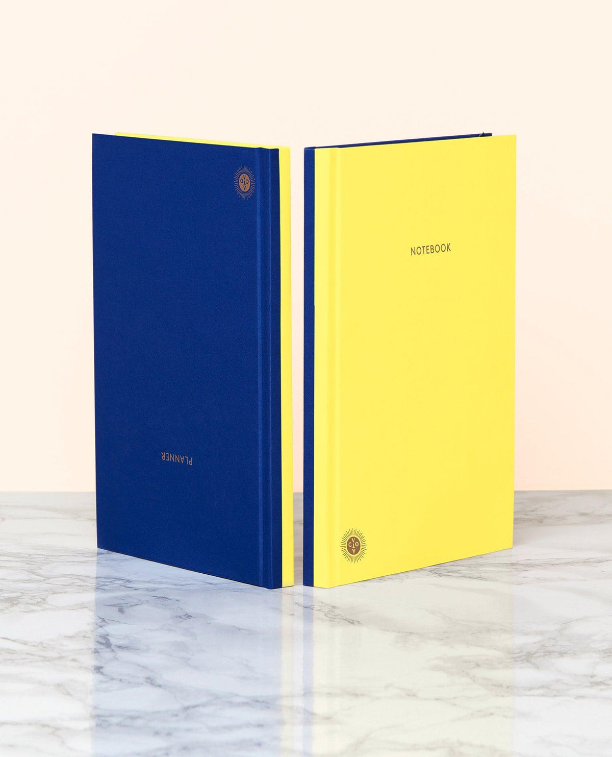 Two OCTAEVO Notebook Planners, blue and yellow, with lay-flat binding on a marble surface.