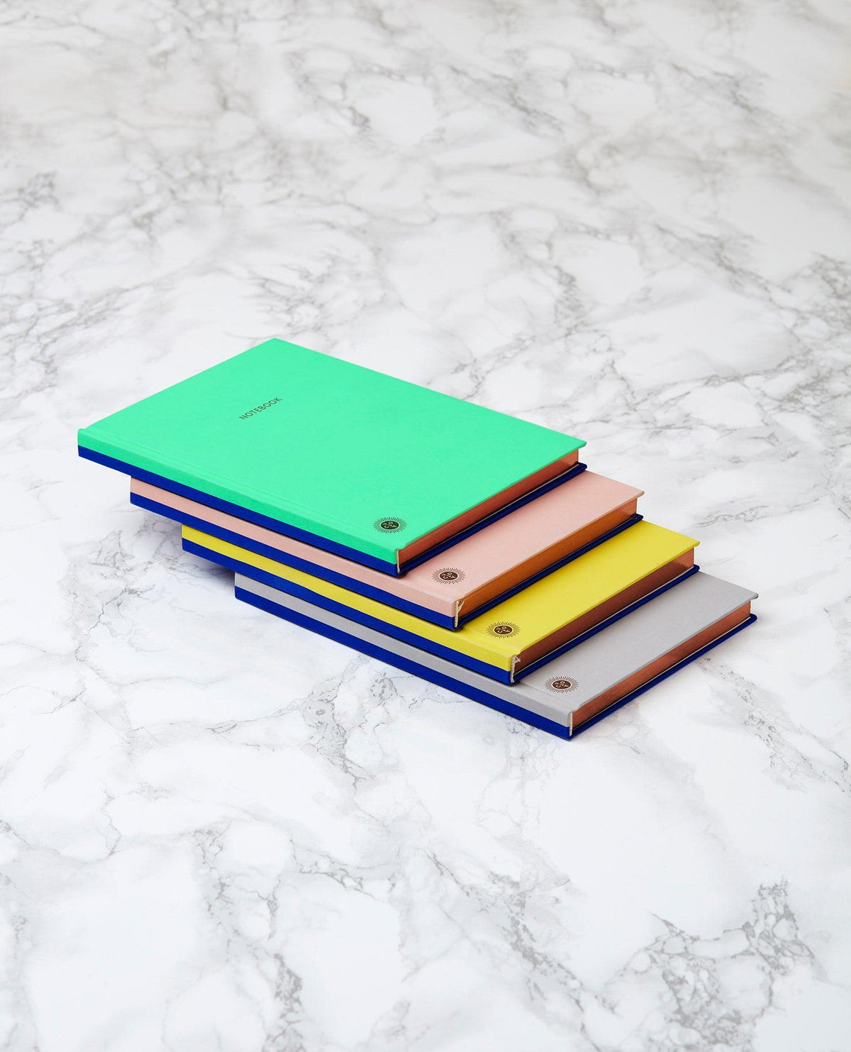 Four OCTAEVO Notebook Planners in several colors are stacked on a white marble surface.