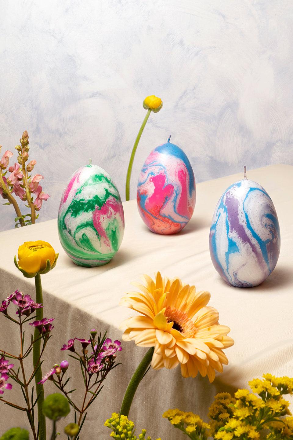 Three Olimpo Marble Candle — Lilac by OCTAEVO sit among flowers on a light, textured backdrop.
