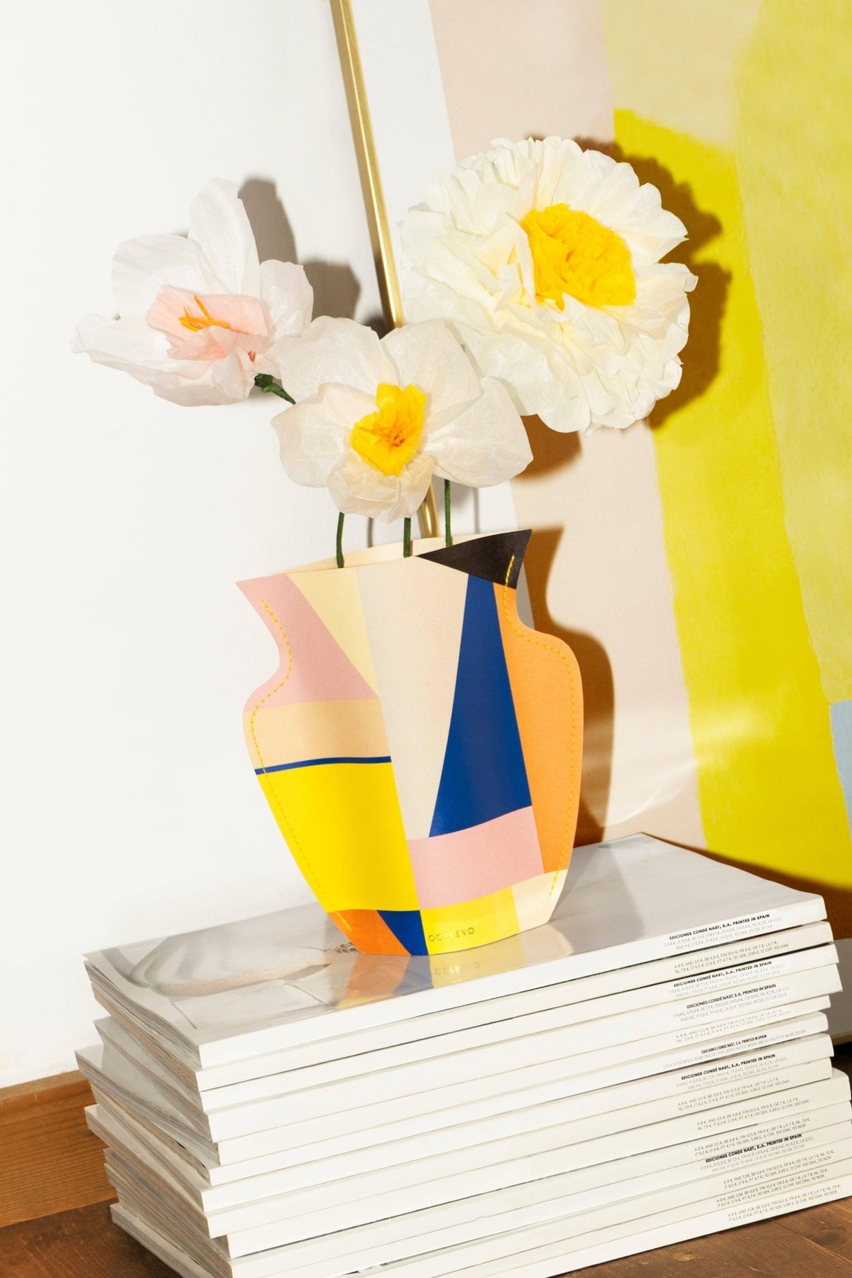 Le bouquet de fleurs en papier Sunrise OCTAEVO est posé sur des magazines, devant un fond blanc et jaune.