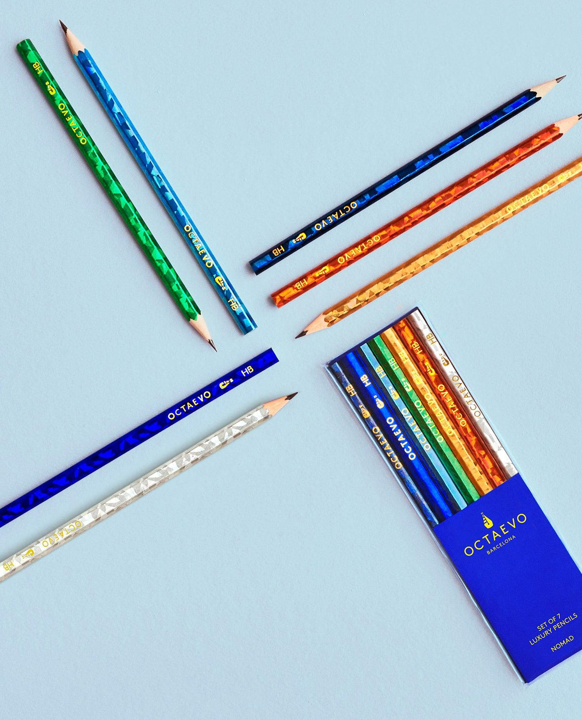 Six NOMAD pencils by Octaevo with an open blue pencil box on a light blue surface.