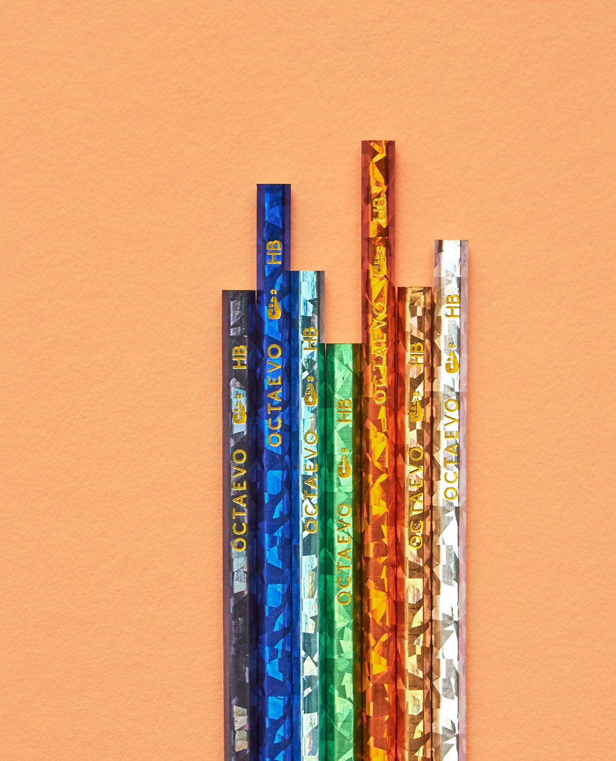 Six Octaevo NOMAD pencils with geometric patterns and gold text stand upright on a peach background.