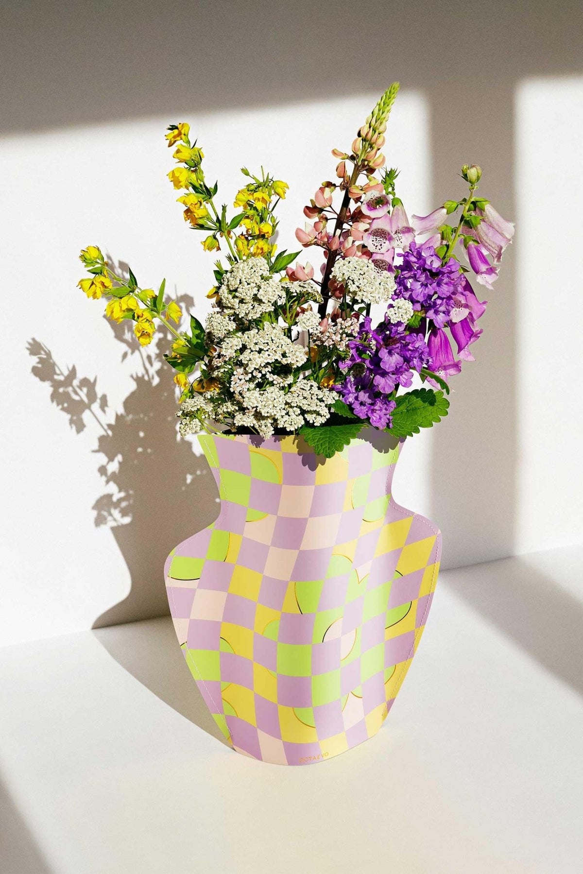 The Octaevo Picnic Paper Vase in a pastel checkerboard design holds wildflowers on a white surface.