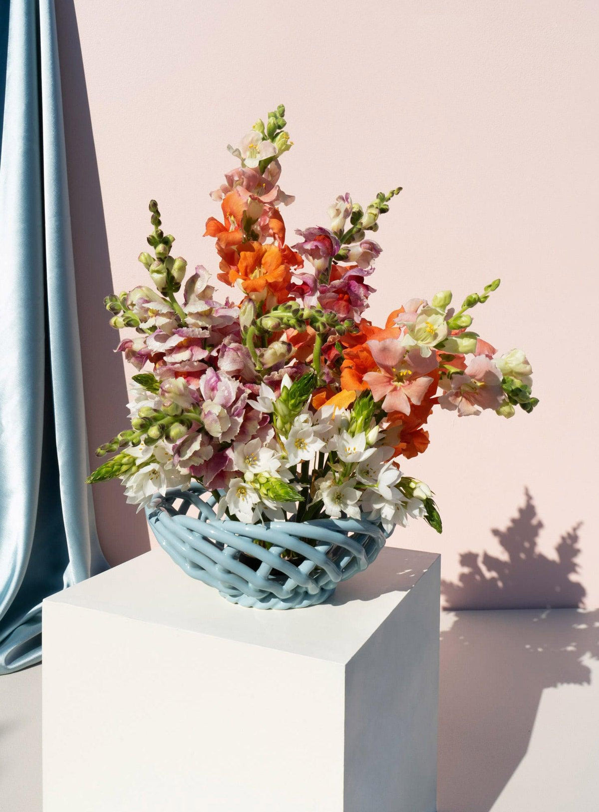 The OCTAEVO Sicilia Ceramic Basket — Small holds orange, pink, and white flowers on a pedestal, pale pink background.