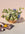 An orange ceramic basket with wildflowers sits next to a soft cloth on a pale surface.