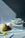 The OCTAEVO Sicilia Ceramic Basket displays yellow lemons and cantaloupe on blue fabric in dramatic lighting.