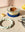 A baked custard dessert in a glass dish on a light mint trivet, with a lemon, a roll, and a vanilla bean nearby.
