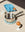 A saucepan, eggs, light blue OCTAEVO Sicilia Ceramic Trivet, egg cup, and glass of milk on a beige surface in bright light.