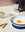 A bowl, toast, egg, butter, and a stovetop espresso maker sit on a blue OCTAEVO Sicilia Ceramic Trivet.