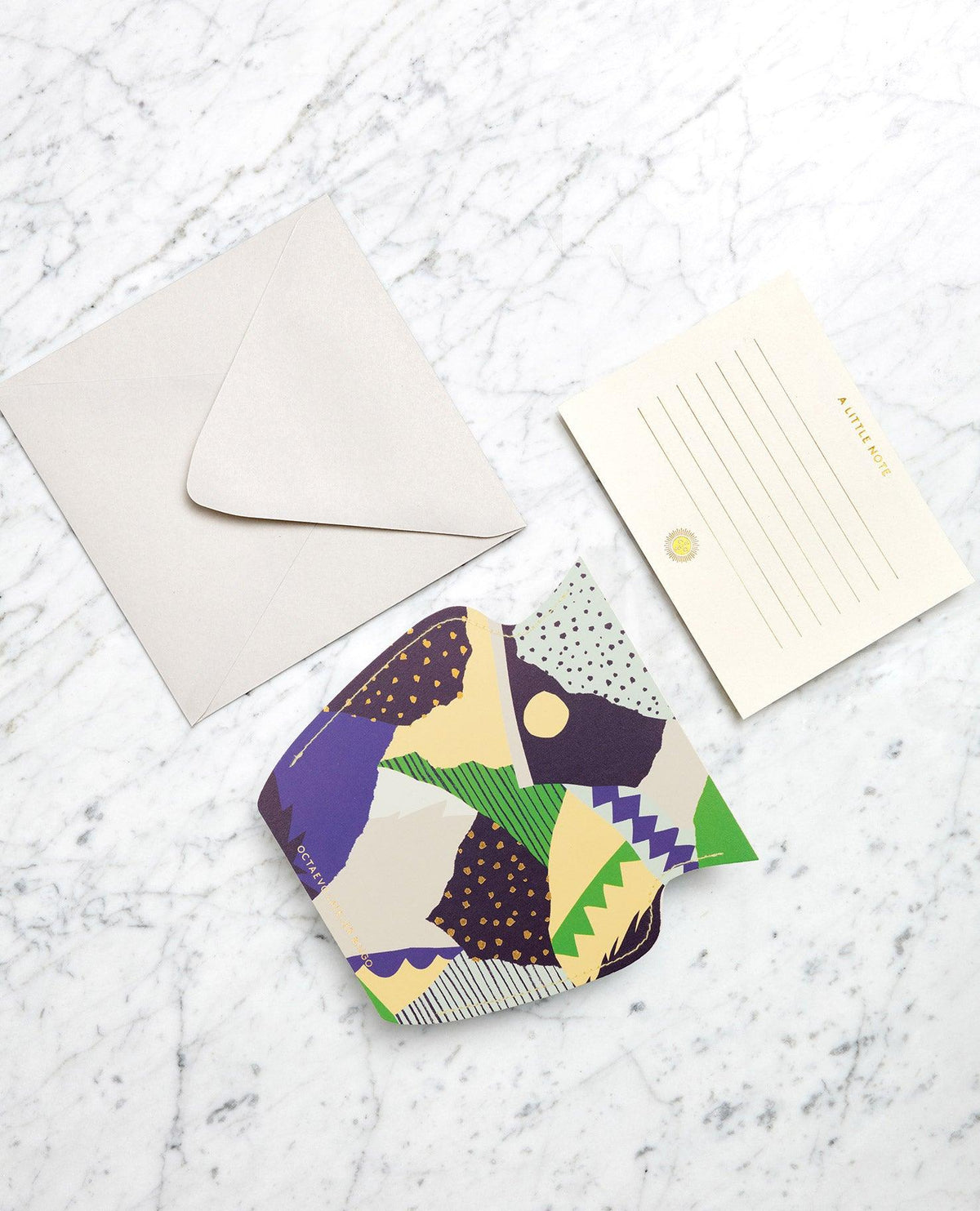 The Stromboli Mini Paper Vase by OCTAEVO sits on white marble next to a gold-lined notecard and blank envelope.