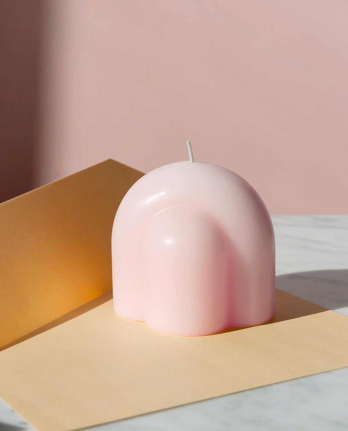 The Templo Candle by OCTAEVO, artisan-made and pink, sits on beige paper with a pastel pink background.