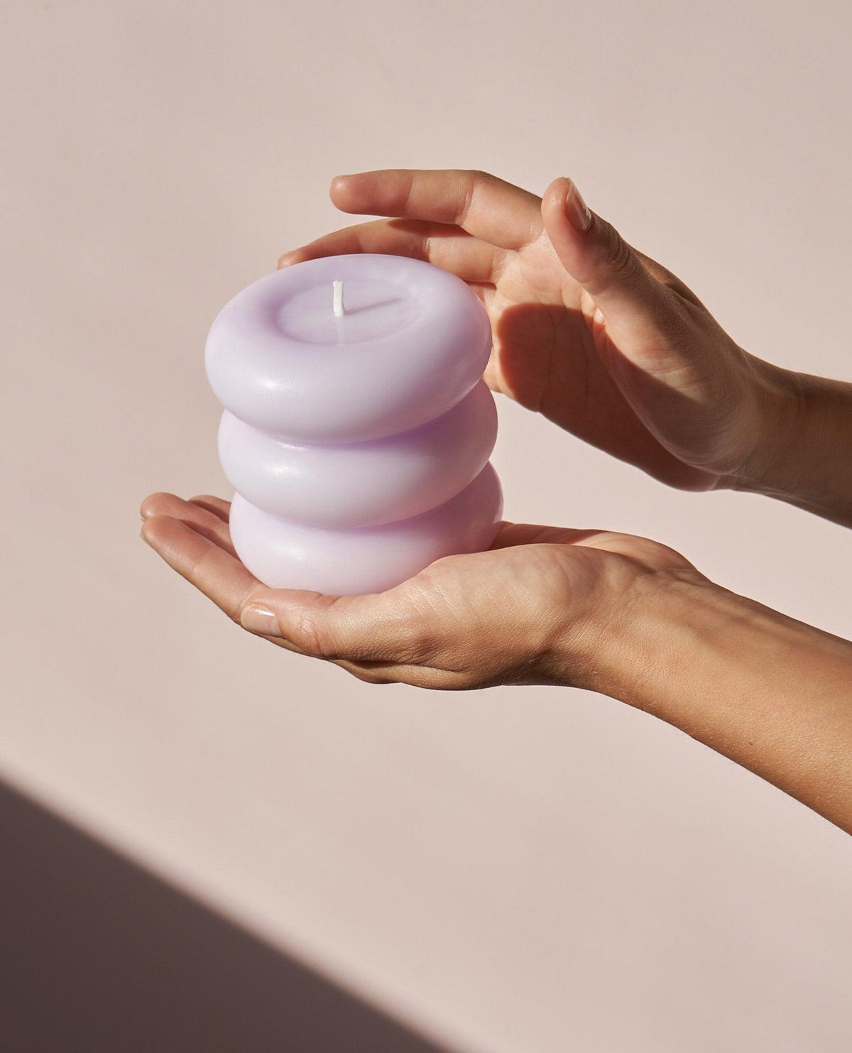 Hands hold the Templo Candle — Pale Lilac by OCTAEVO, an artisan sculpture, against a soft pink background.