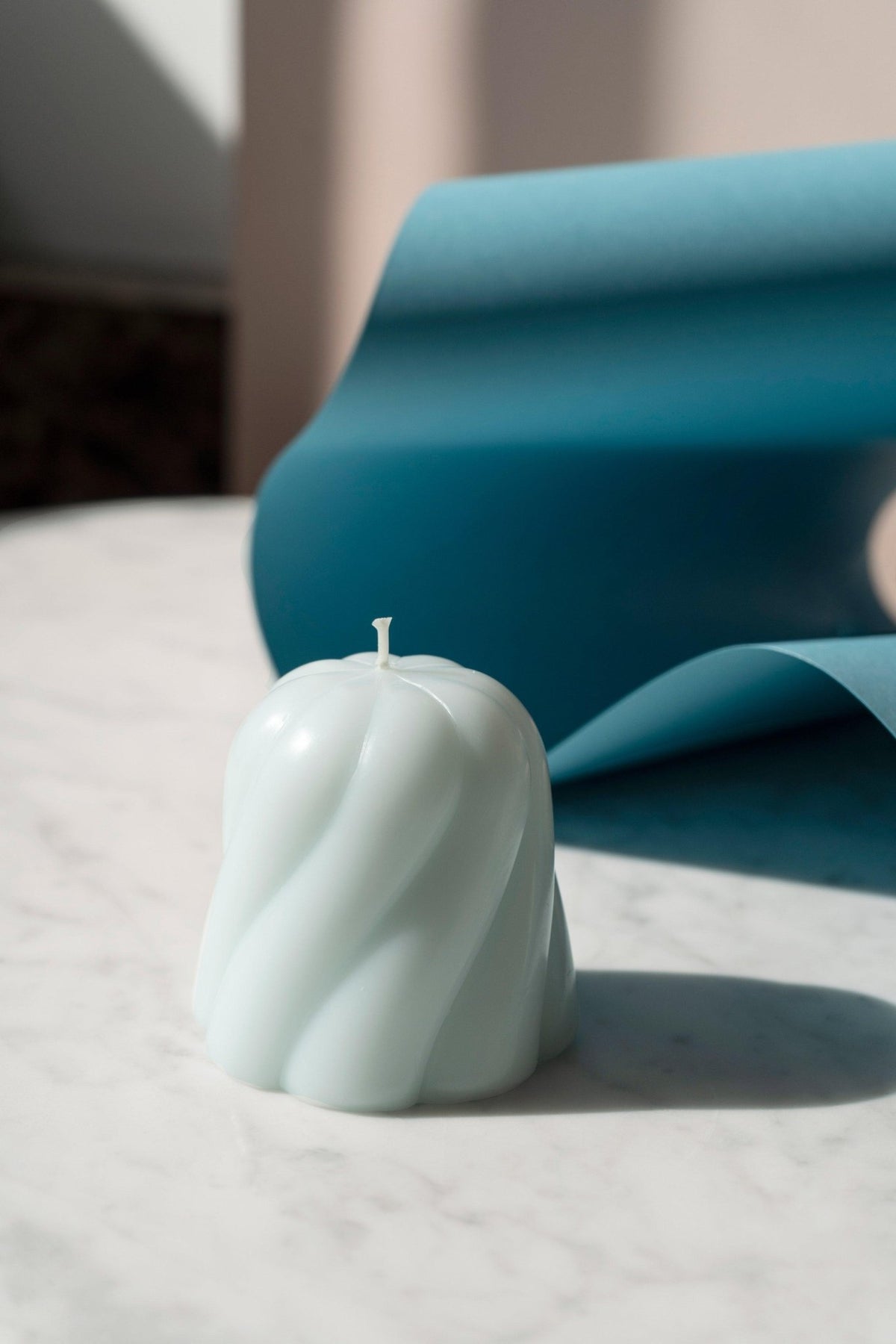 The OCTAEVO Templo Candle in Light Blue rests on marble before a blue backdrop, sculpted like a twisted dome.