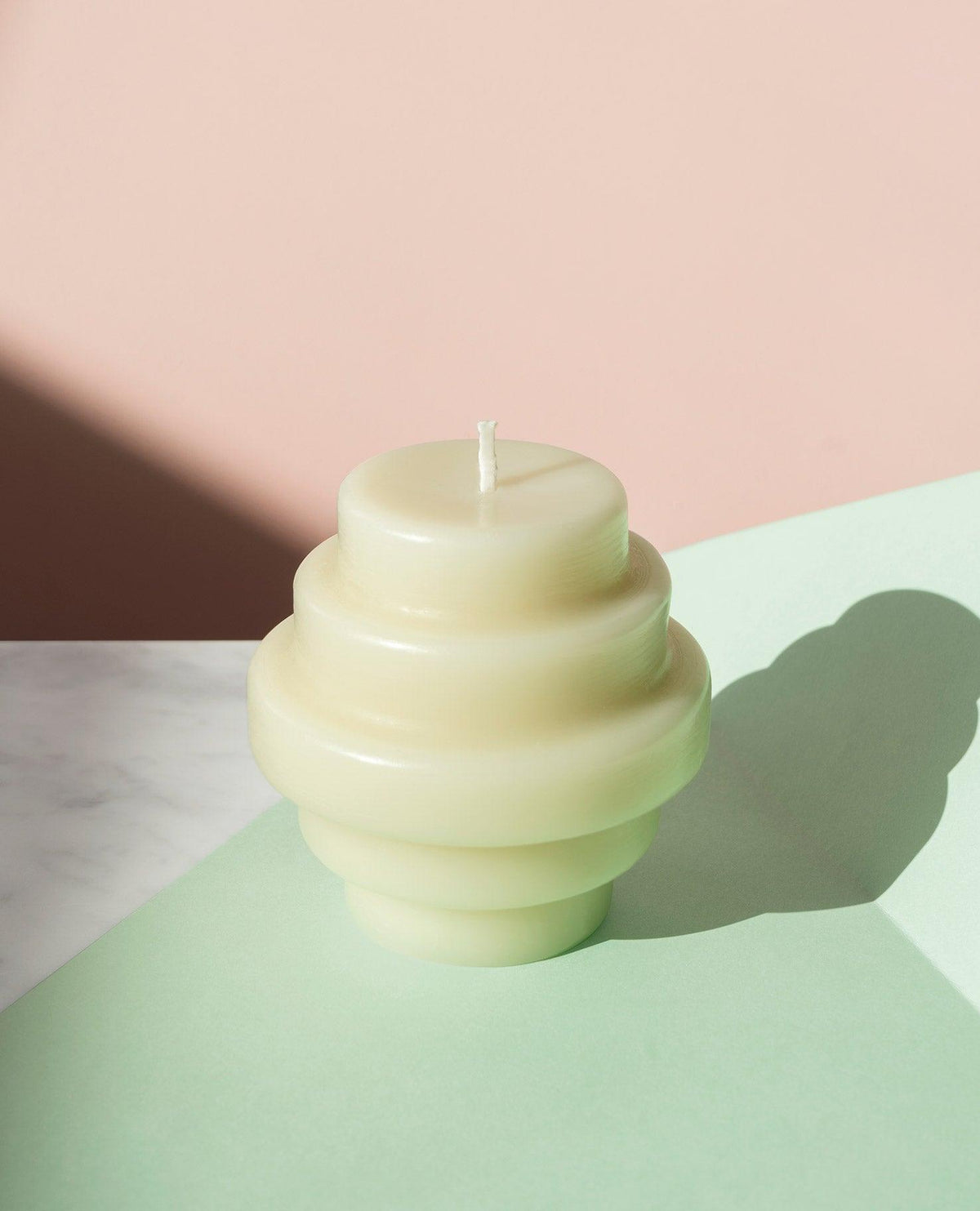The Templo Candle by OCTAEVO, a sculpted tiered artisan piece, rests on a pastel surface with a soft pink backdrop.
