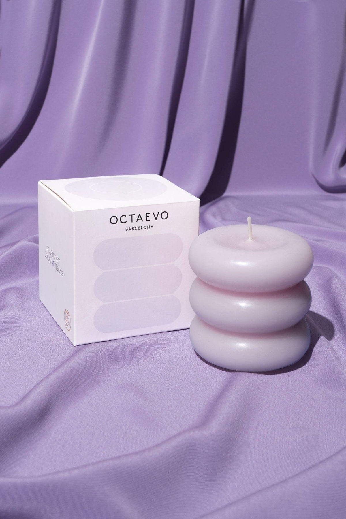 OCTAEVO's Templo Candle — Pale Lilac, with its box, rests on silky lavender fabric with delicate folds.