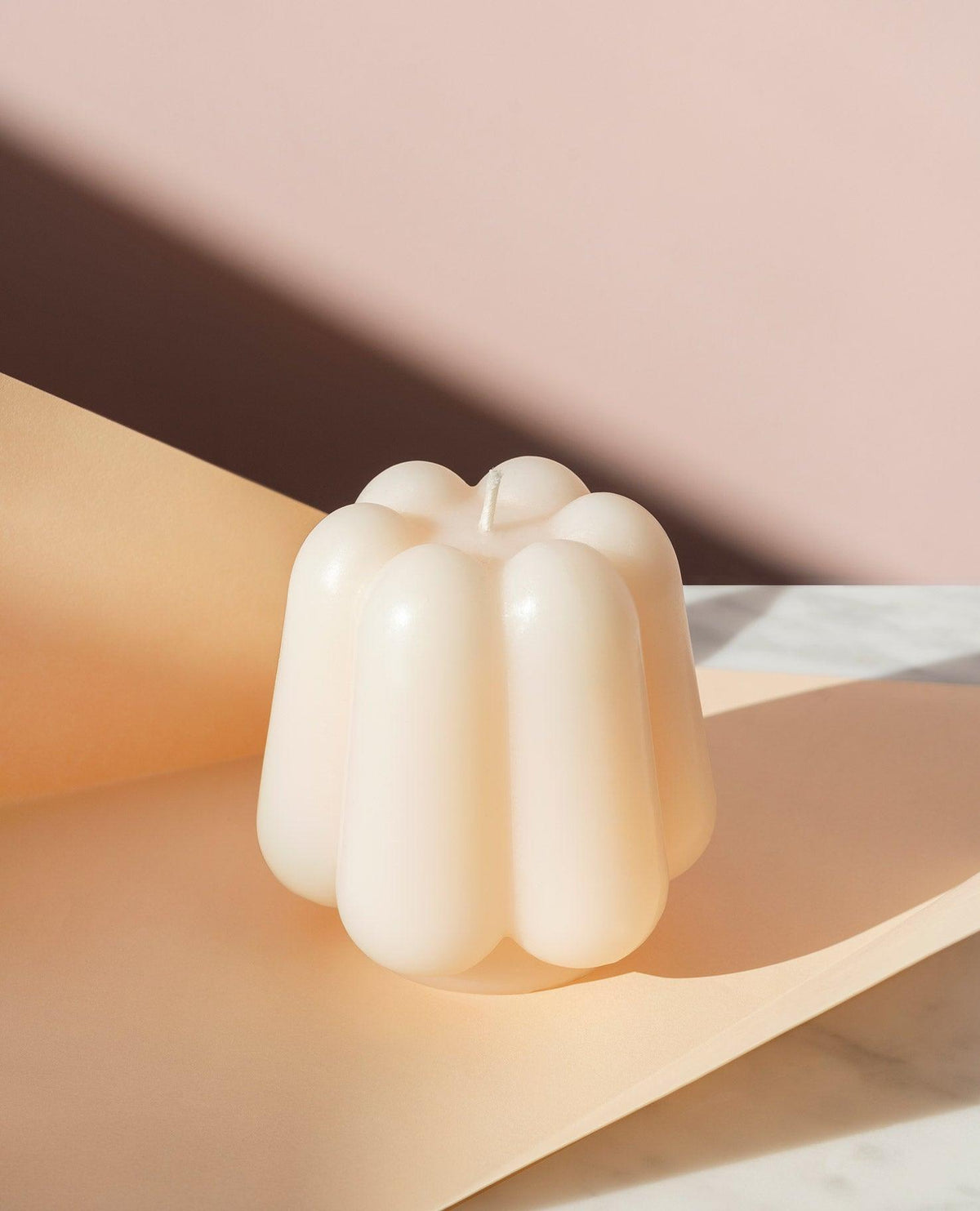 The Templo Candle by OCTAEVO—a white sculpted wax piece—rests on peach paper with a soft pink backdrop.
