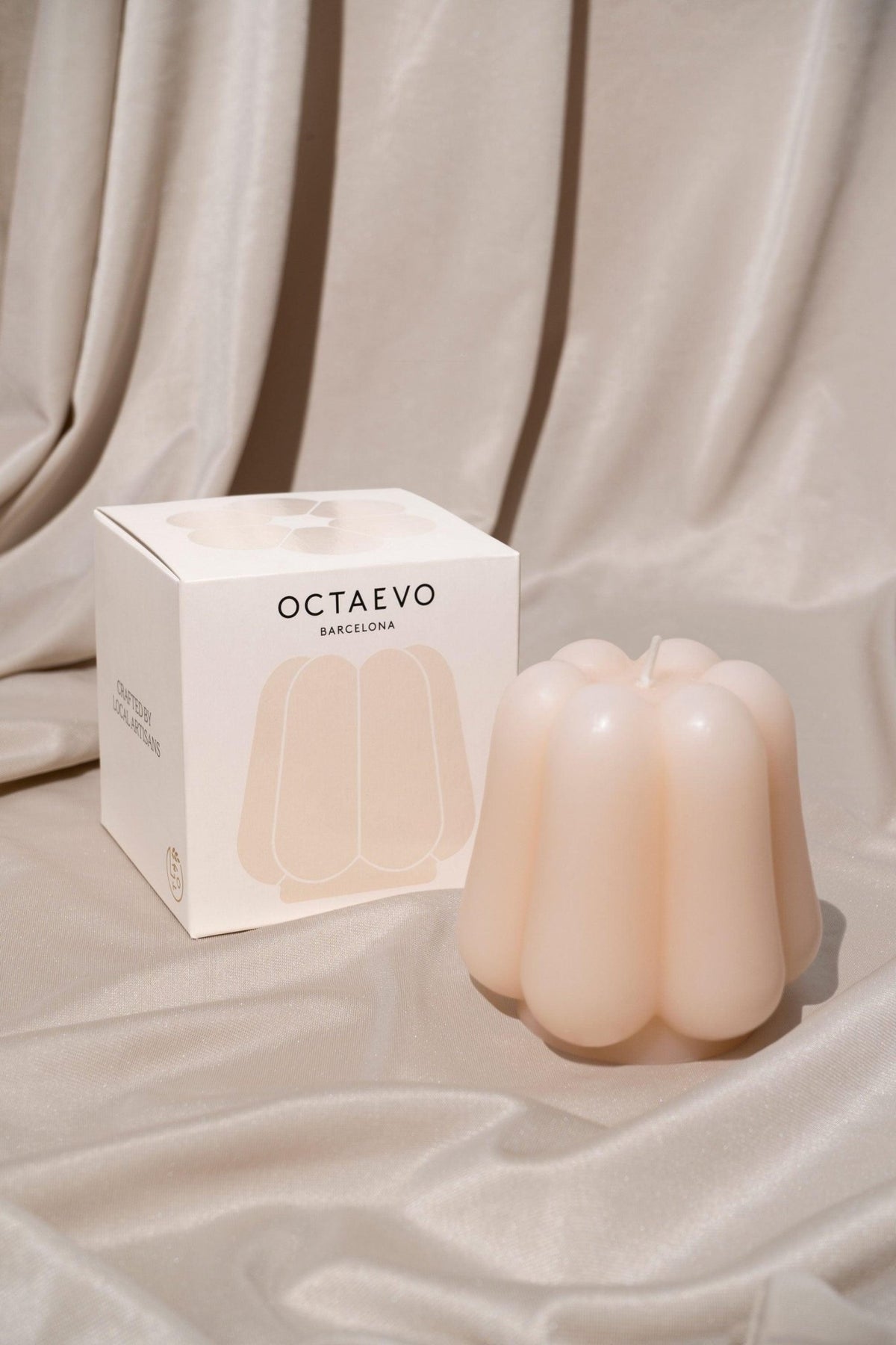 The OCTAEVO Templo Candle — Ivory rests by its box on silky beige fabric, artisan-crafted and hand poured.