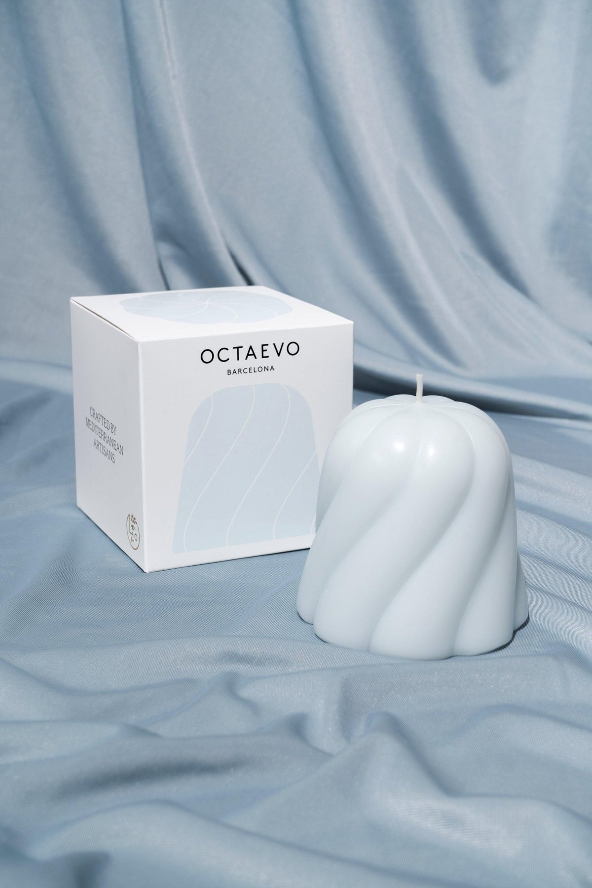 Light blue Templo Candle by OCTAEVO, a handmade Italian sculptural piece, shown on matching blue fabric.