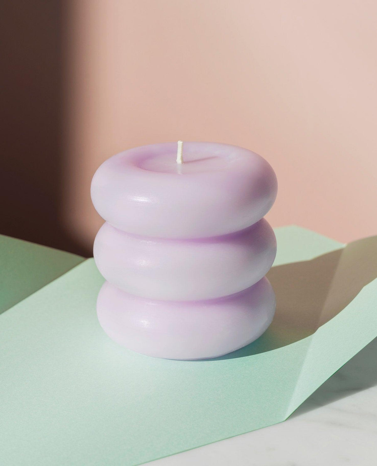 The OCTAEVO Templo Candle, a pastel purple three-tiered design, rests on mint and white with a pink backdrop.