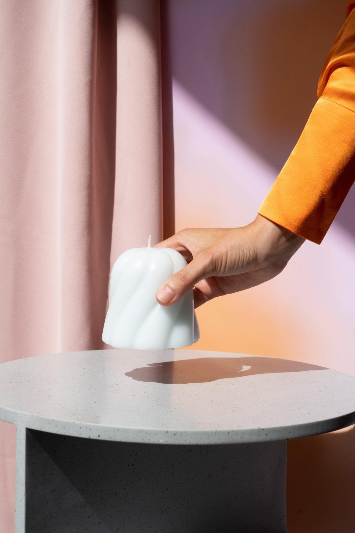 A hand in an orange sleeve places the white Octaevo Templo Candle on a round, light gray table.