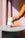 A hand in an orange sleeve places the white Octaevo Templo Candle on a round, light gray table.