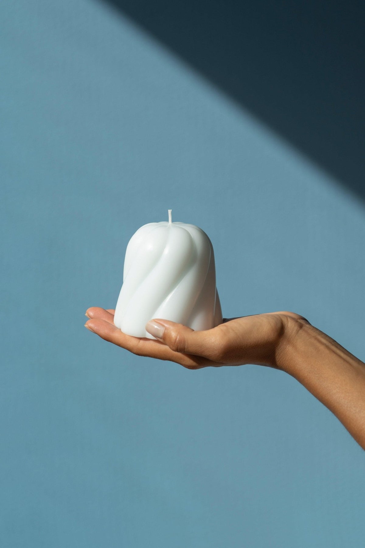 A hand holds the OCTAEVO Templo Candle in light blue against a blue background with a striking diagonal shadow.