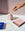 A hand lights the pink, dome-shaped Templo Candle by OCTAEVO with a match beside two matchboxes on marble.