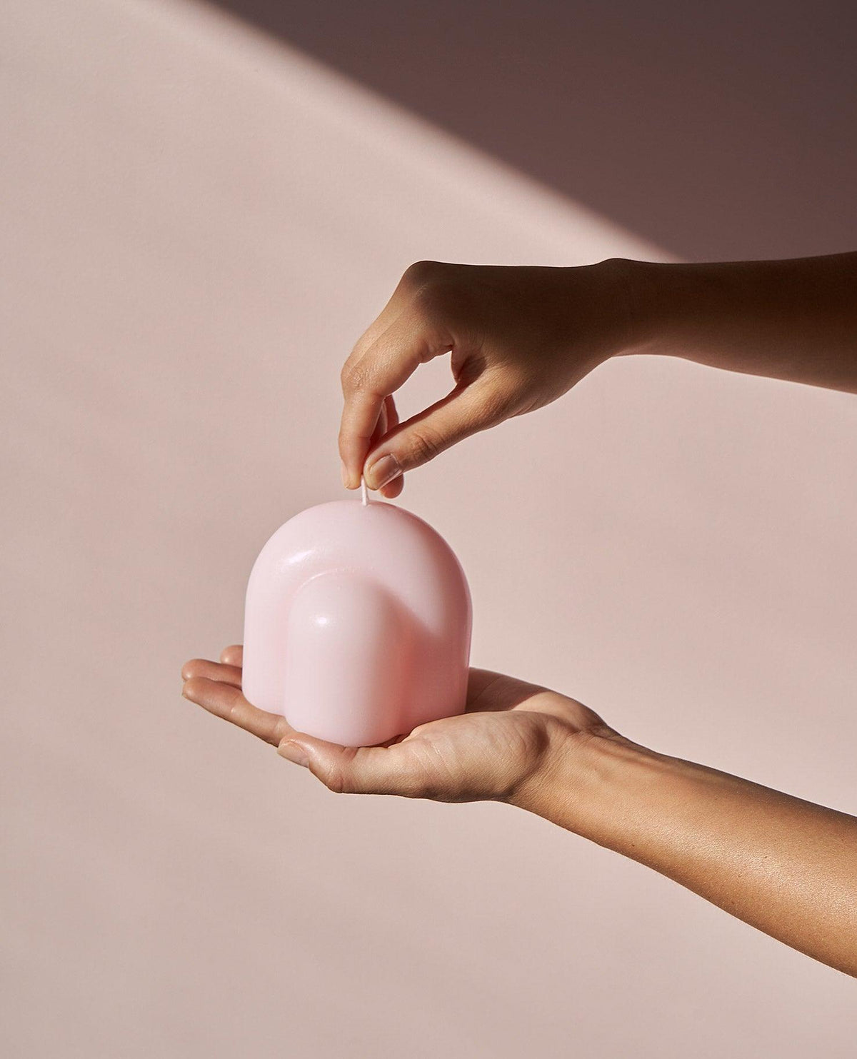 Two hands hold OCTAEVO’s Templo Candle — Pale Rose, an arch-shaped wax sculpture, against a soft pink background.