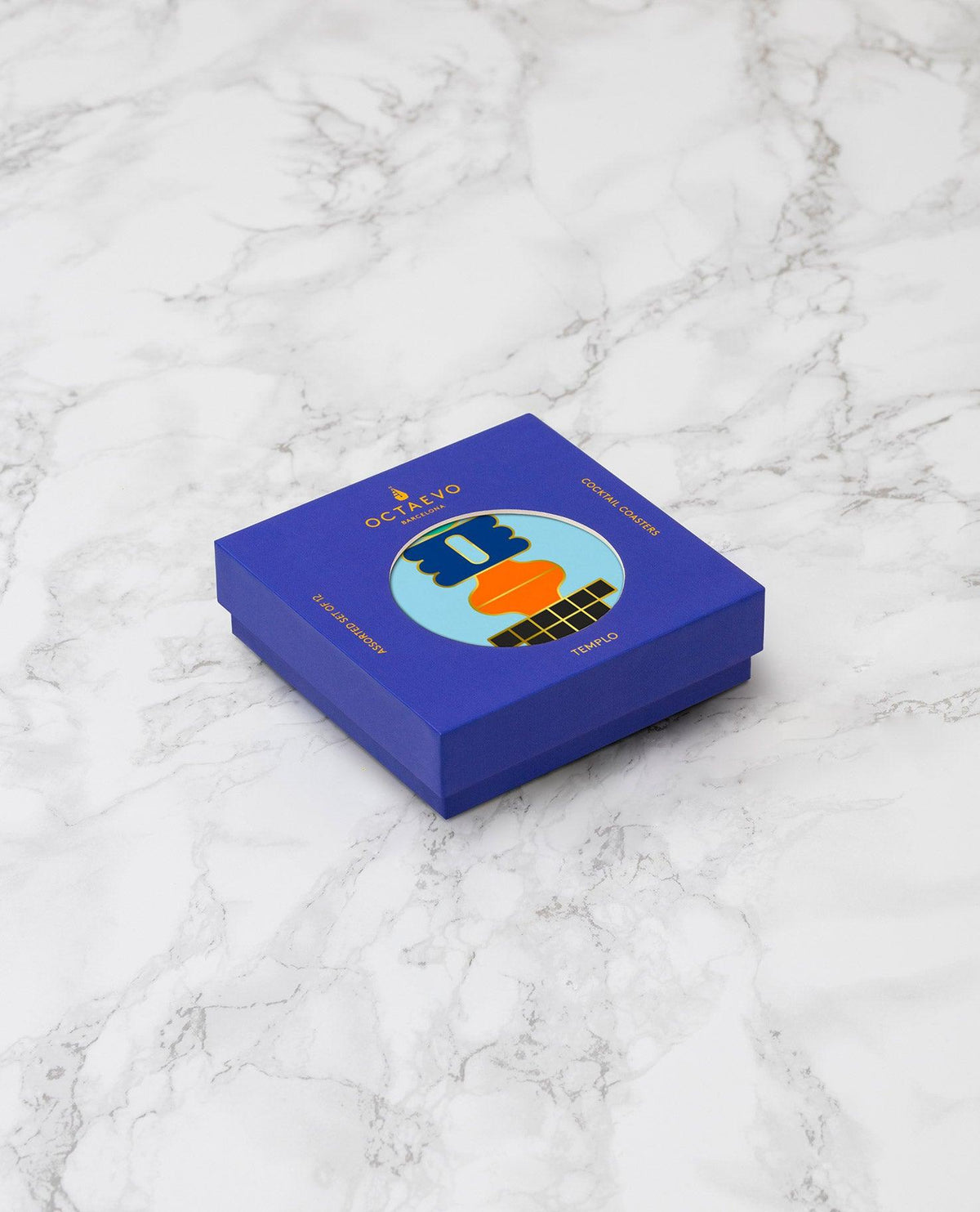 Templo Cocktail Coasters by OCTAEVO in a blue gift box with colorful abstract art and gold foil on the lid, set on marble.